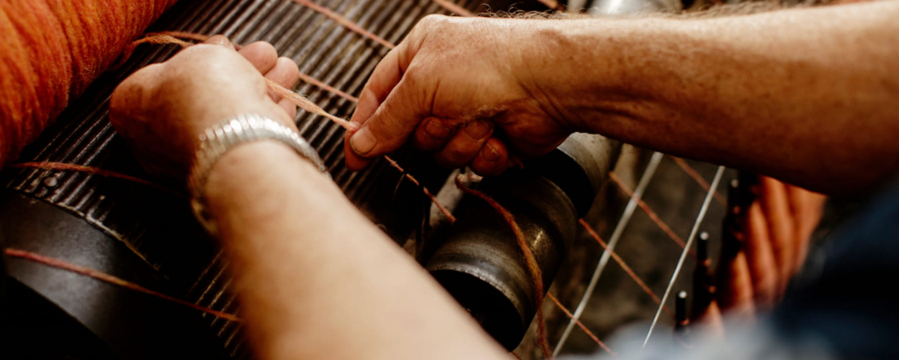 Hands pulling orange wool threads on a loom