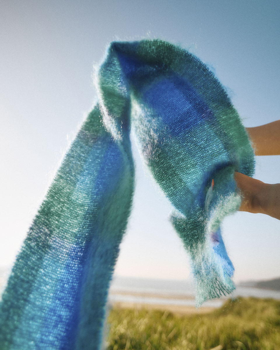 Blue and green tartan scarf flowing through the air against a light blue sky and sandy beach background