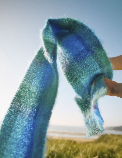 Blue and green tartan scarf flowing through the air against a light blue sky and sandy beach background