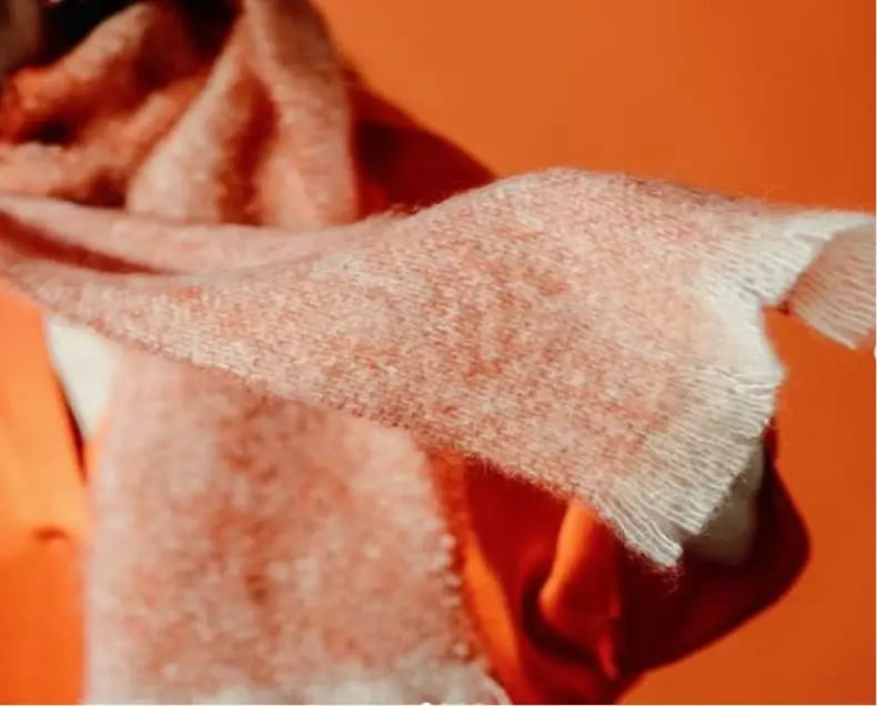 Pale orange woollen scarf blowing in the wind against a bright orange backdrop